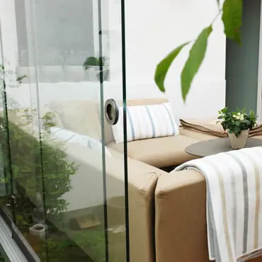 Glasschiebetür als Windschutz auf Terrasse mit gemütlicher Outdoorcouch und kleinem Tisch im Hintergrund.