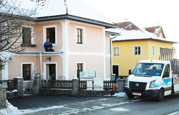 Ein Monteur bereitet die Montage einer Glasueberdachung an einem Wohnhaus vor. Ein Montagefahrzeug steht davor, die Szene zeigt eine typische Baustellensituation im Winter.