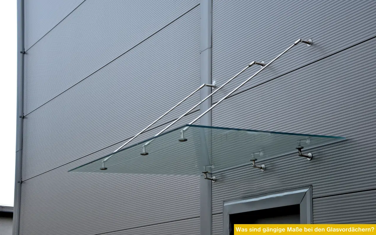 Ein modernes Glasvordach mit Edelstahl-Abhängungen an einer anthrazitfarbenen Metallfassade.