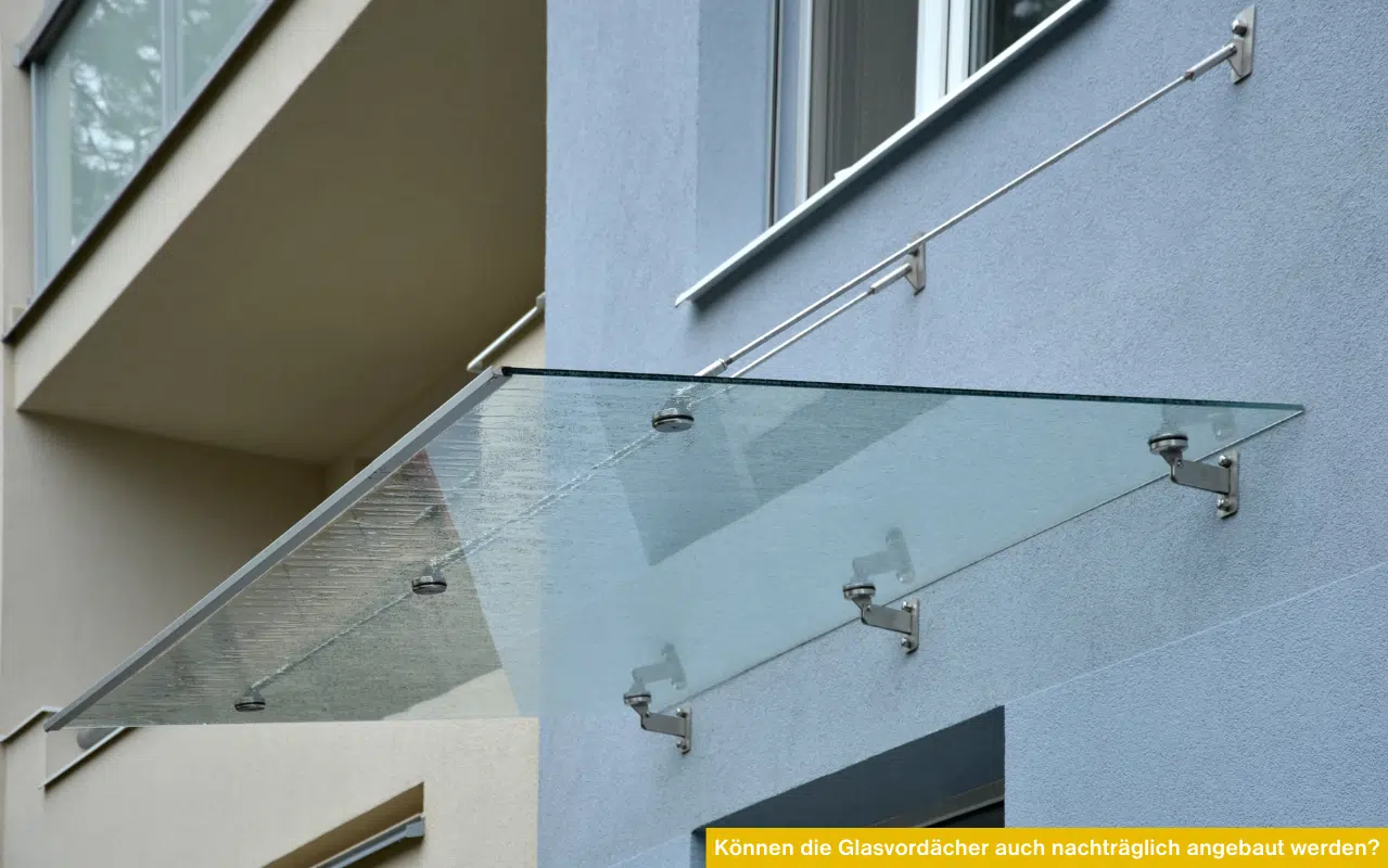 Ein modernes Glasvordach mit Edelstahl-Zugstangen, nachträglich montiert an einer hellblauen Hausfassade.