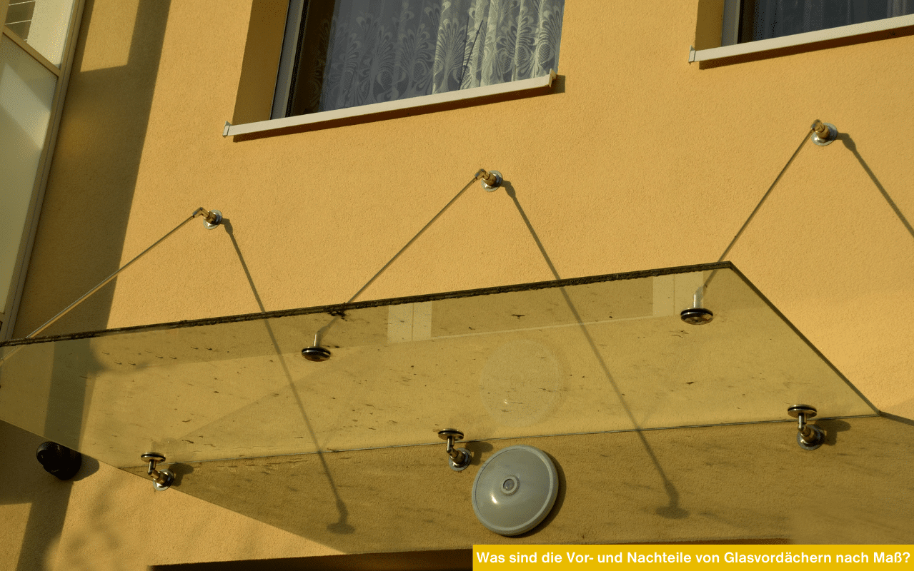 Ein rahmenloses Glasvordach mit drei Edelstahl-Punktfaltern und Abhängungen an einer gelben Hausfassade.