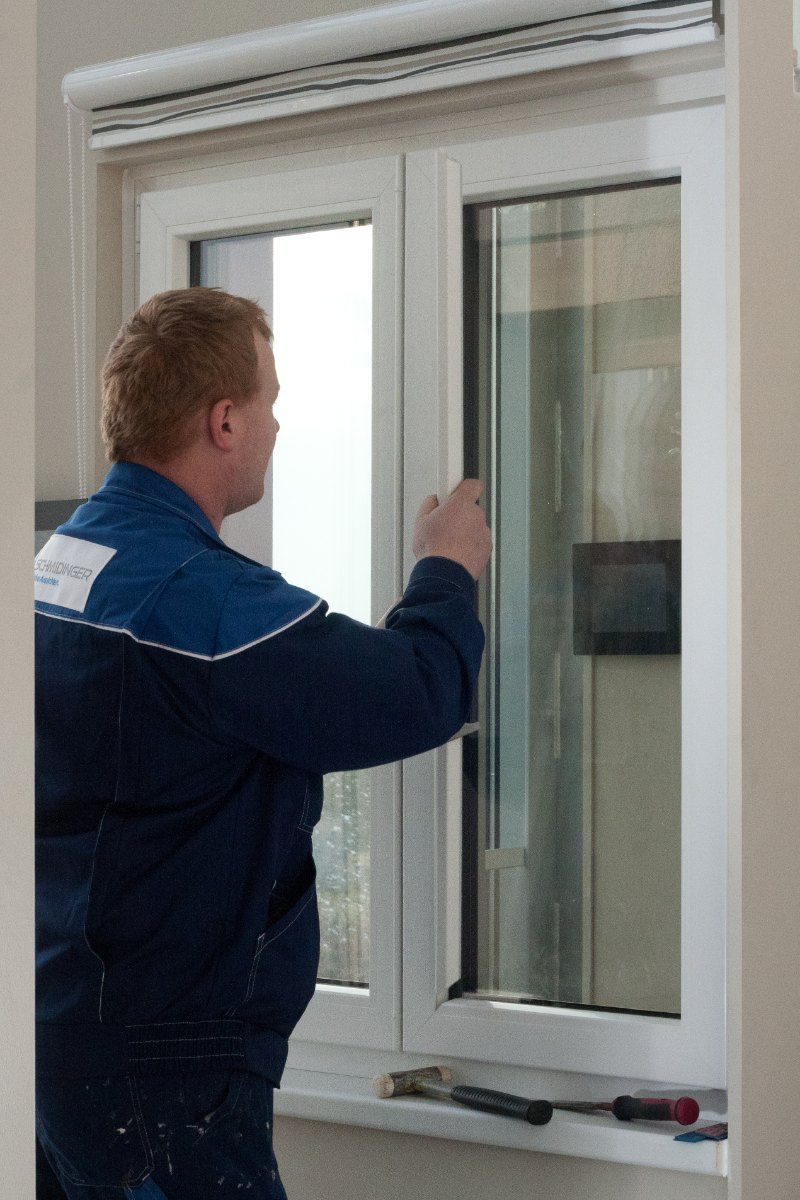 Glaser prüft ein weißes Kunststofffenster vor dem Glaswechsel