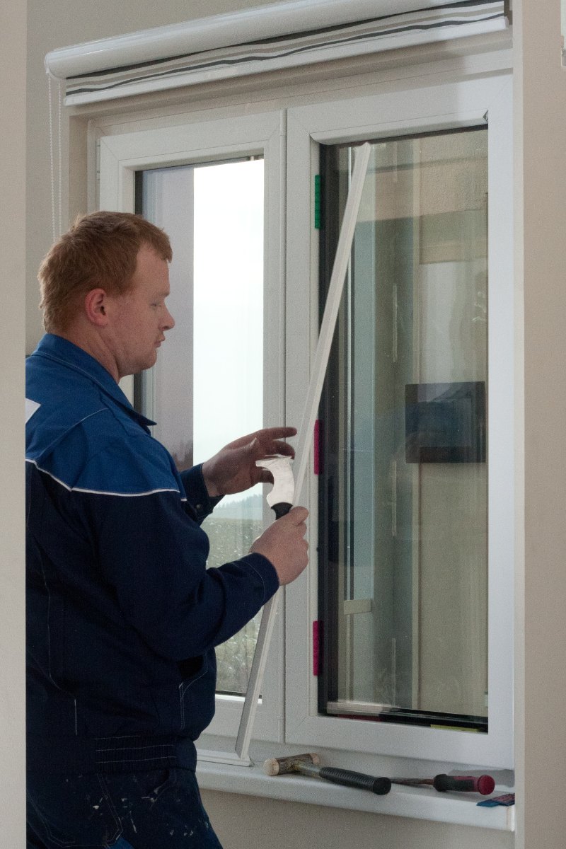 Glaser zieht die lange senkrechte Glasleiste aus dem Kunststofffensterflügel