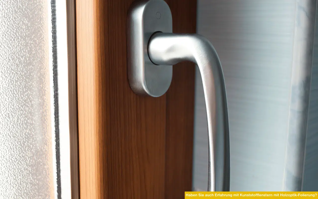 Nahaufnahme eines modernen Fenstergriffs aus Metall an einem Kunststofffenster mit Holzoptik-Folie.