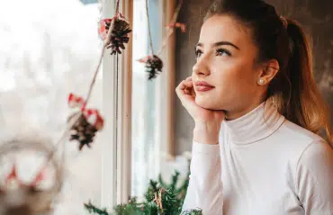 Frau am Kunststoff-Fenster denkt über häufige Probleme und deren Lösungen nach.