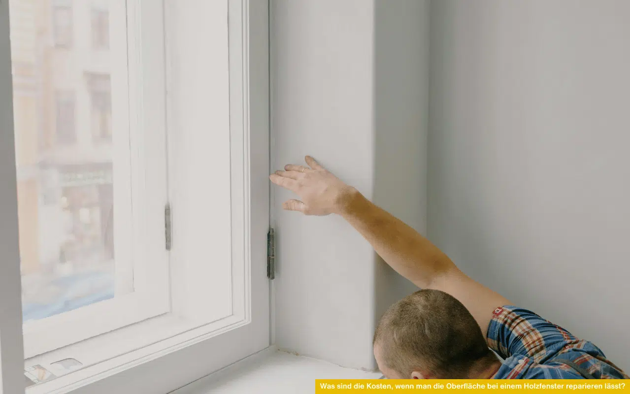 Handwerker prüft weiß lackiertes Holzfenster innen – was sind die Kosten, wenn man die Oberfläche bei einem Holzfenster reparieren lässt.