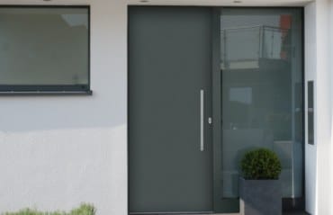 Moderne Haustür in Dunkelgrau mit großem verglastem Seitenteil und Stangengriff an einem weißen Haus