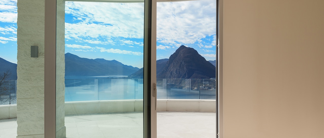 Eine Hebeschiebetür verbindet modernen Wohnraum mit einer Terrasse und bietet freie Sicht auf einen See und Berge. Sie veranschaulicht die Vorteile lichtdurchfluteter Räume und großzügiger Öffnungen.
