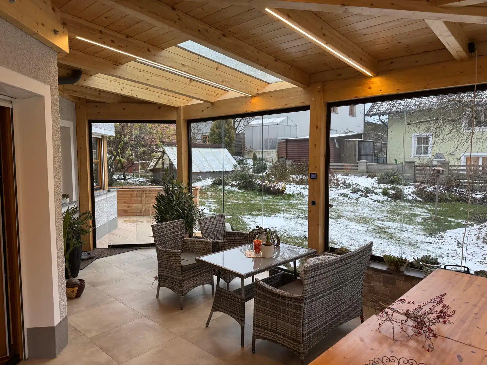 Holzanbau mit rahmenlosen Glasschiebetüren als geschützter Terrassenbereich