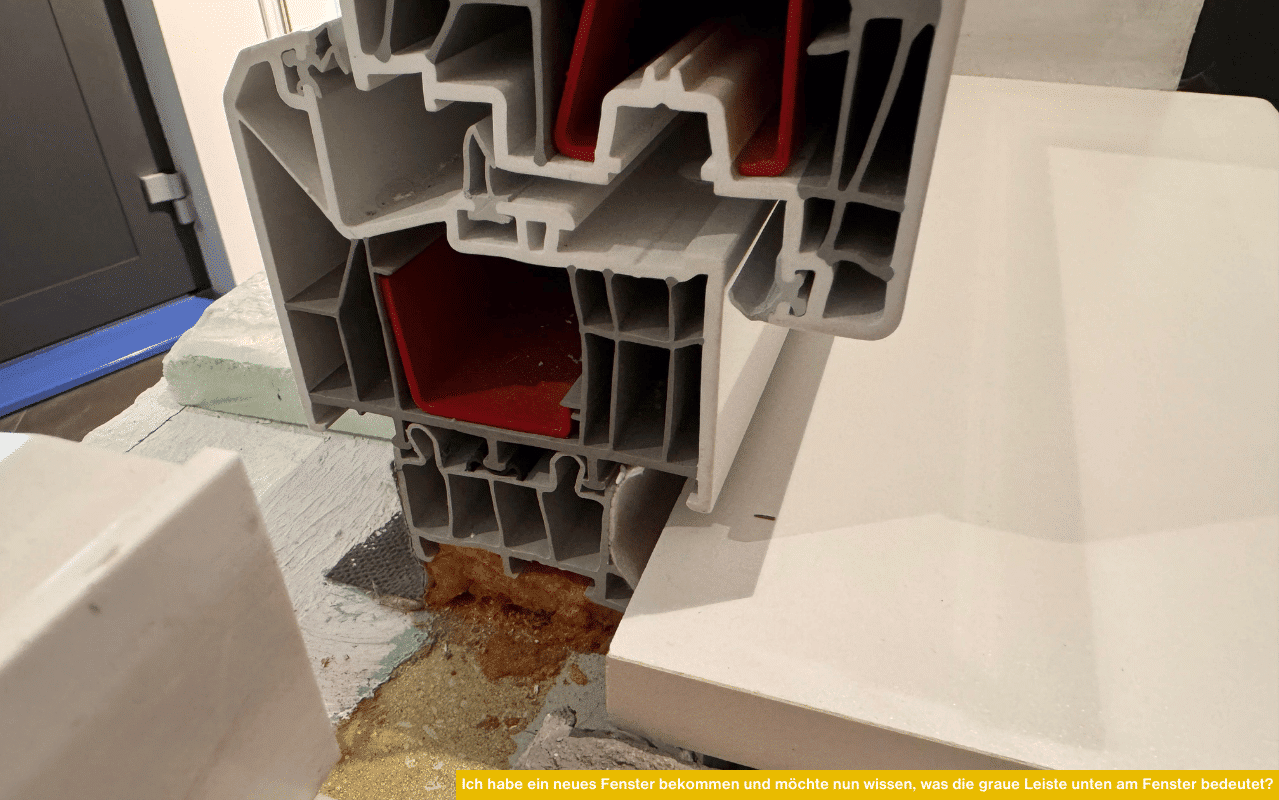 Detailaufnahme eines modernen Fensterprofils mit roter Verstärkung und grauer Leiste im unteren Bereich des Rahmens.