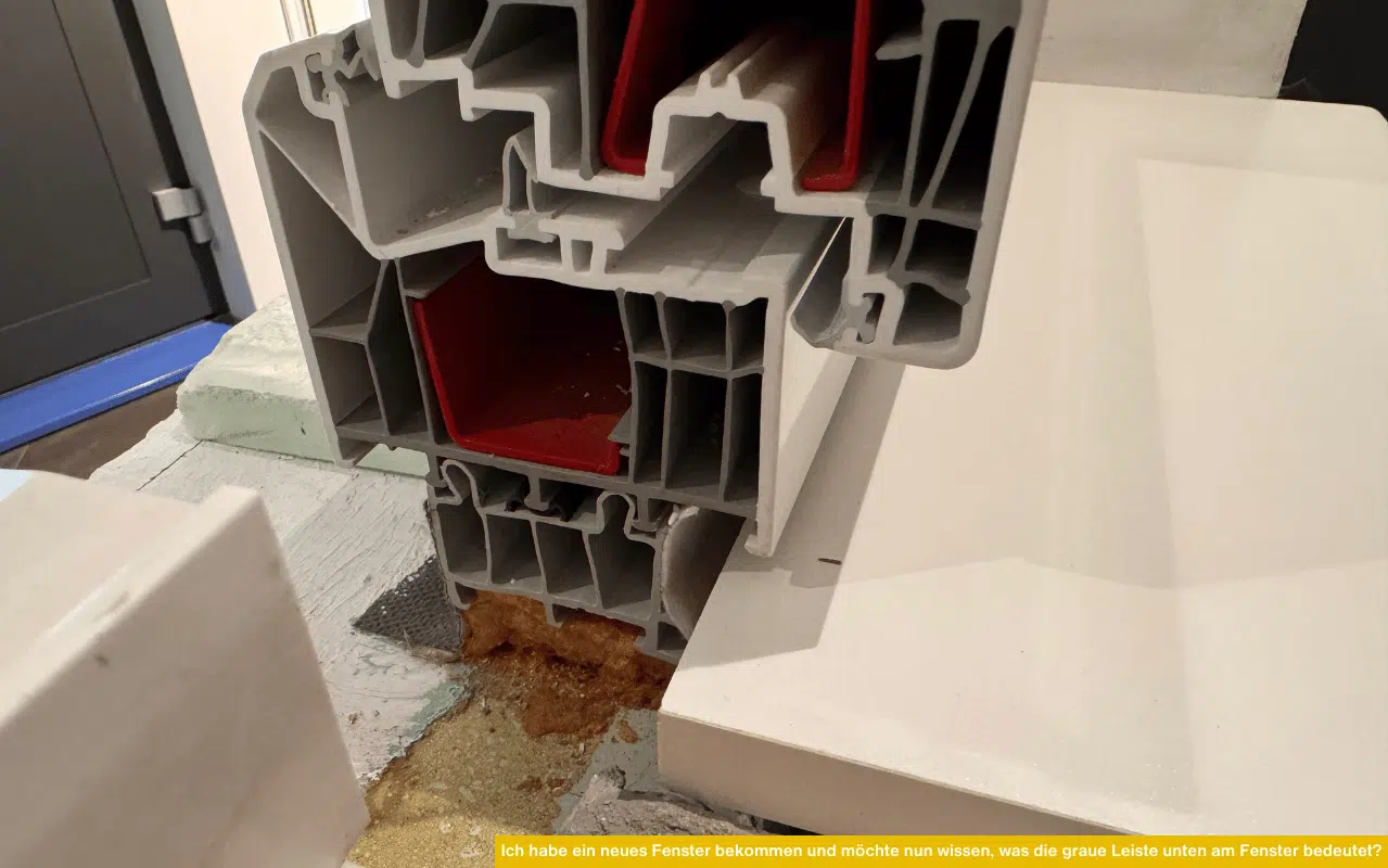 Detailaufnahme eines modernen Fensterprofils mit roter Verstärkung und grauer Leiste im unteren Bereich des Rahmens.