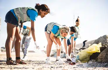 Junge Menschen sammeln Plastikabfall am Strand für innovative Rollos aus Plastik-Müll.