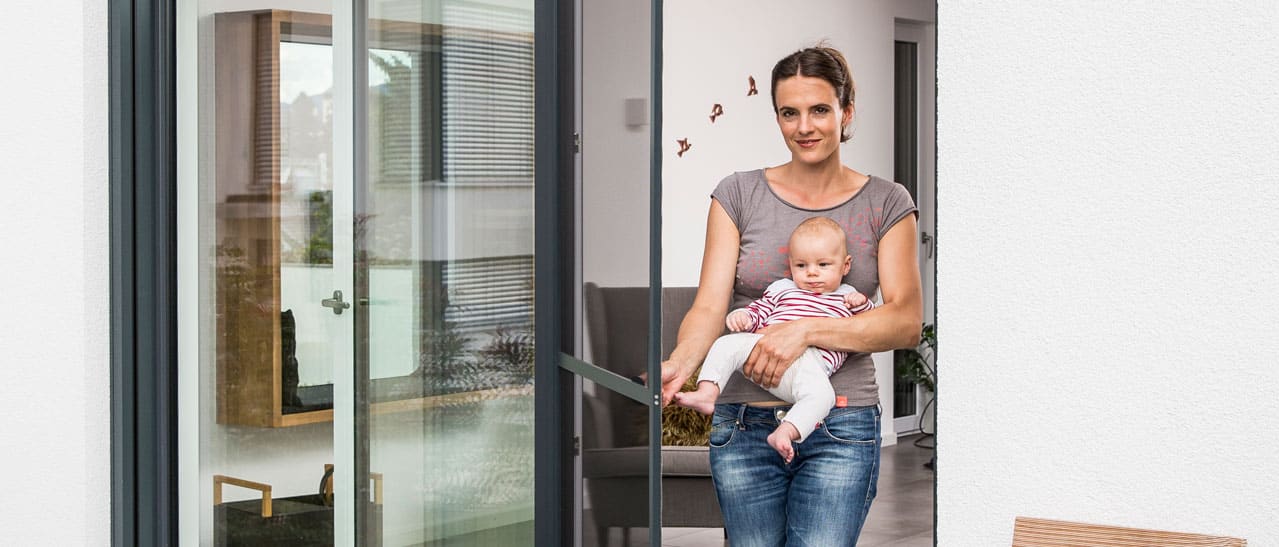 Frau öffnet mit einer Hand kinderleicht den Insektenschutzdrehrahmen an Balkontüre.