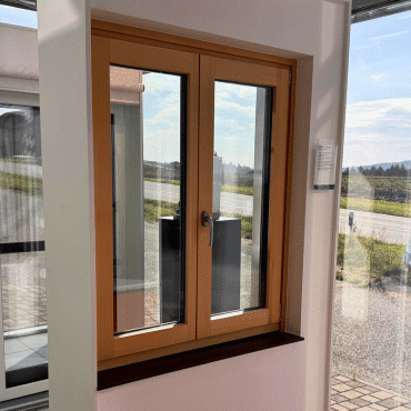 Doppelflügeliges Isolierglasfenster in Holzoptik mit Dreh-Kipp-Beschlag, montiert in einer Musterwand im Schauraum.