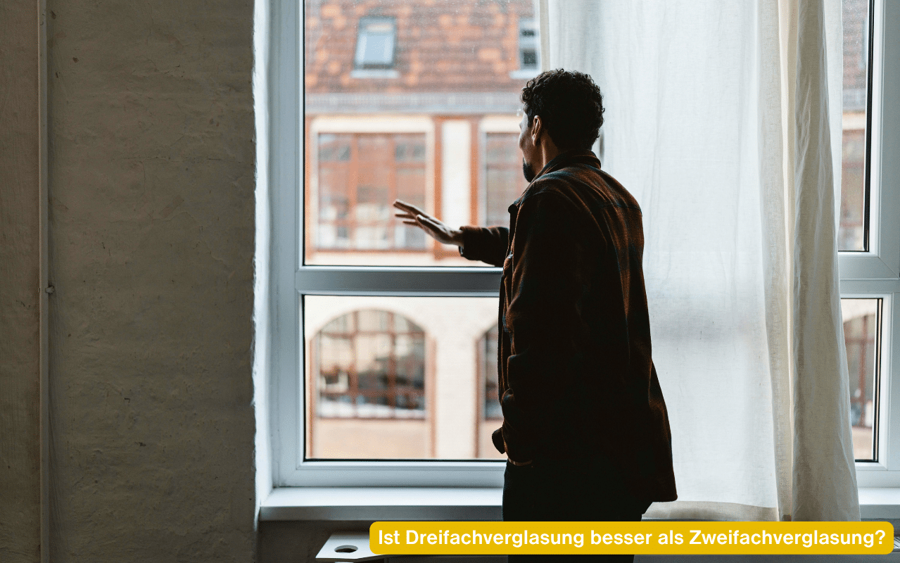 Ist Dreifachverglasung besser als Zweifachverglasung - Person prüft am Fenster die Verglasung mit Blick auf einen Innenhof