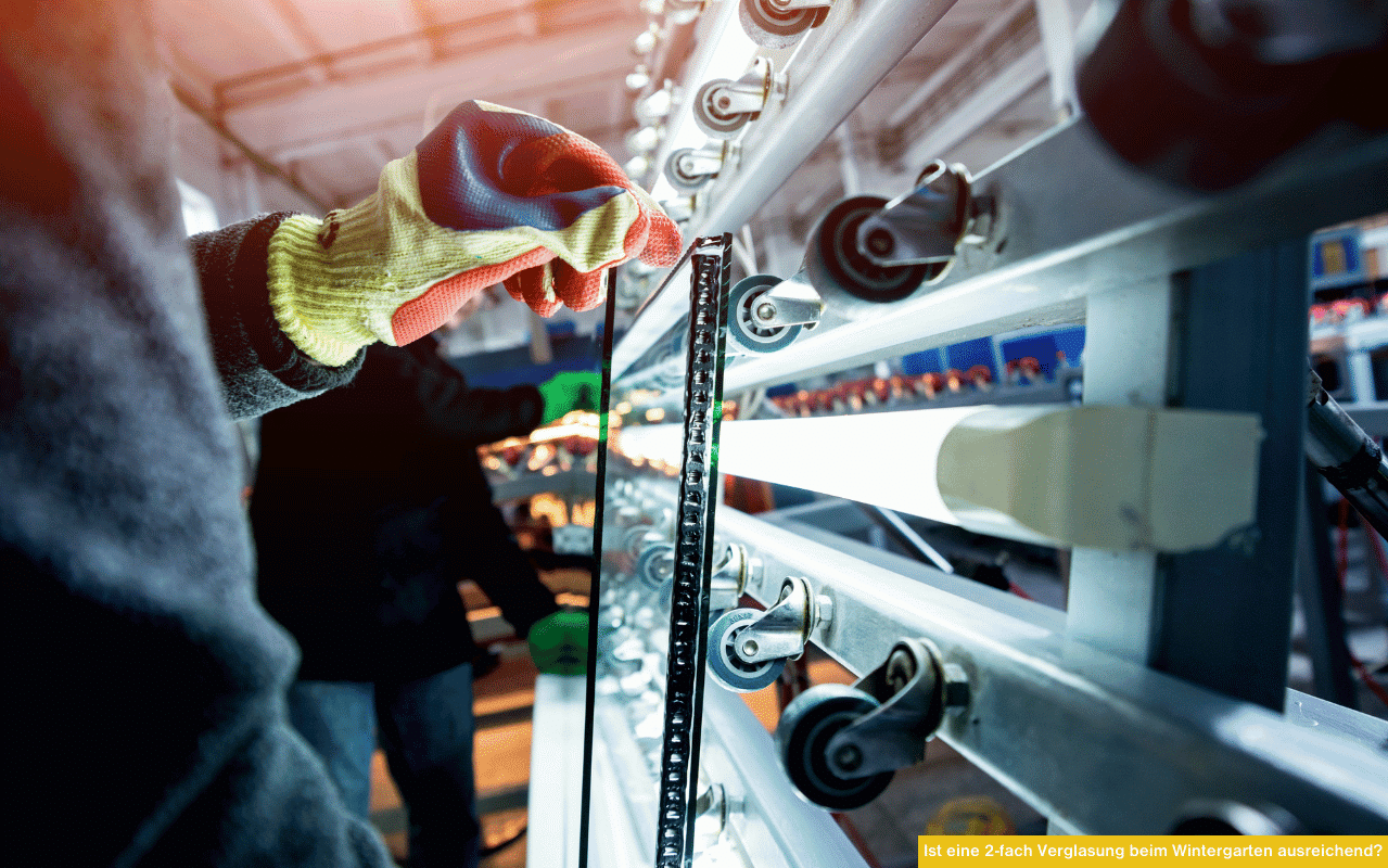 Arbeiter mit Handschuhen hält eine Glasscheibe an einer Produktionsanlage, im Hintergrund weitere Glasfertigung sichtbar.