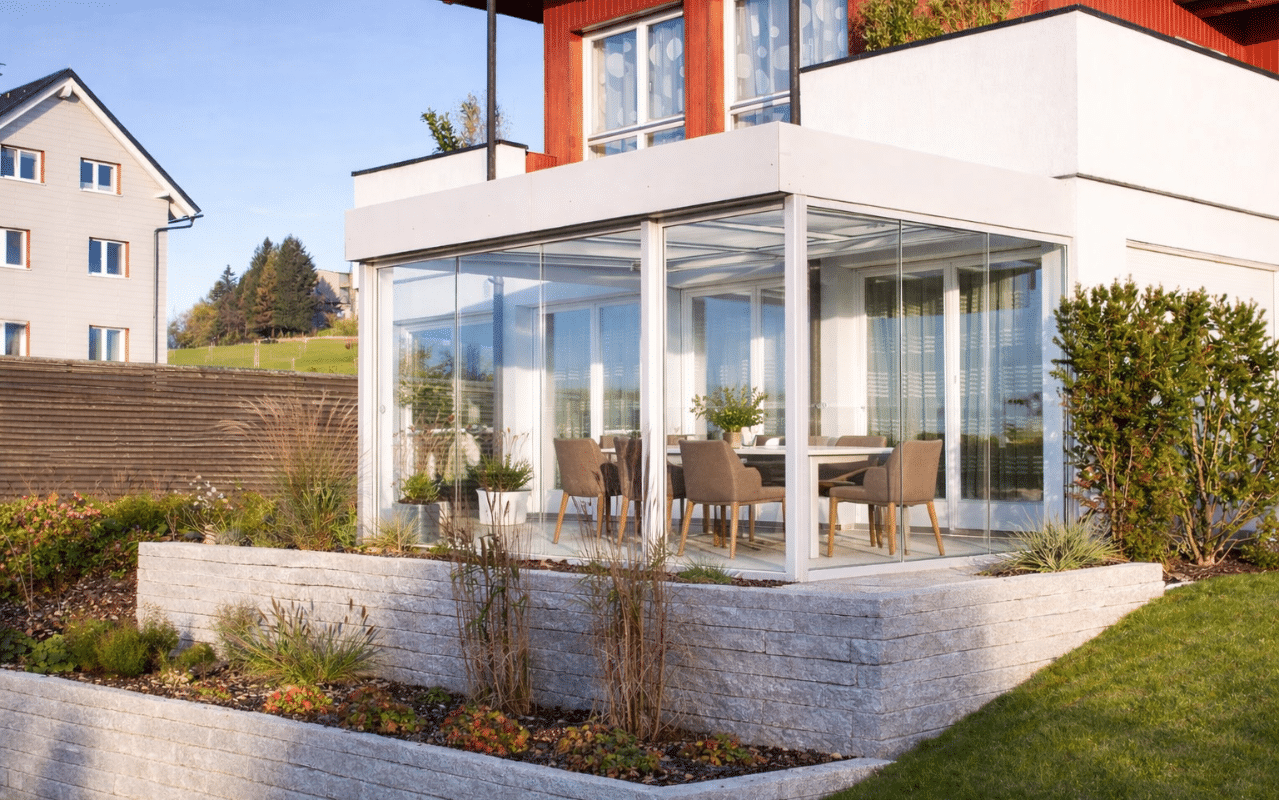 Kaltwintergarten als gläserne Terrassenüberdachung an einem modernen Wohnhaus mit Garten