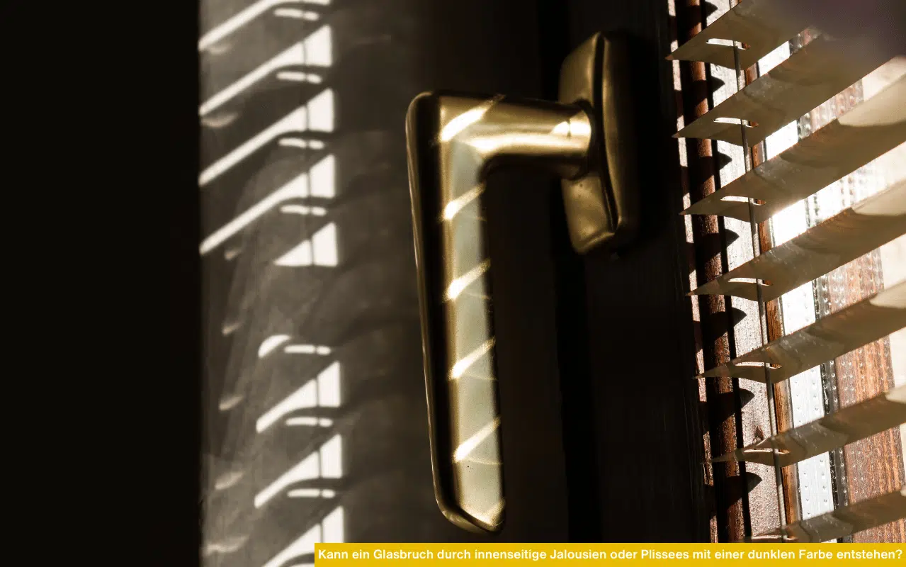 Kann ein Glasbruch durch innenseitige Jalousien oder Plissees mit einer dunklen Farbe entstehen – Sonnenlicht fällt durch dunkle Innenjalousie auf Fenstergriff.