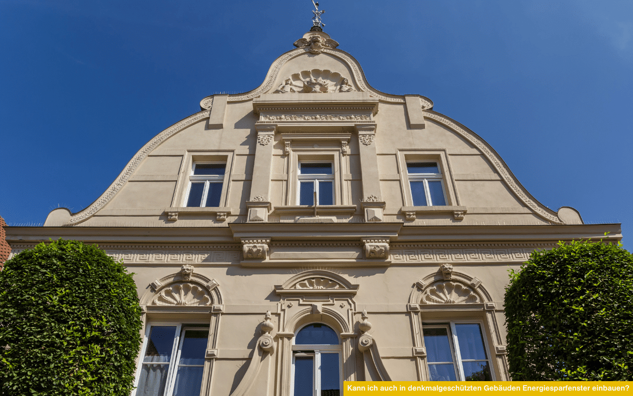 Nahaufnahme einer geschützten Altbaufassade mit Stuck, Giebelornamenten und weißen Fenstern. Die Ansicht verdeutlicht, wie Energiesparfenster gestalterisch an historische Formen angepasst werden können.