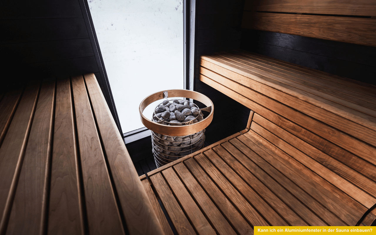 Kann ich ein Aluminiumfenster in der Sauna einbauen? Innenaufnahme einer Sauna mit Holzbank, Saunaofen und Fenster neben dem Ofen.