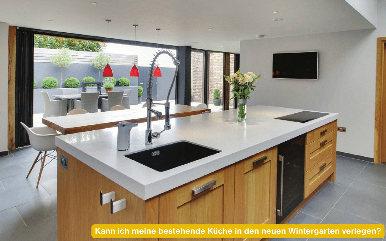 Kann ich meine bestehende Küche in den neuen Wintergarten verlegen? Moderne Küche mit Kochinsel vor einer Glas-Faltwand zur Terrasse