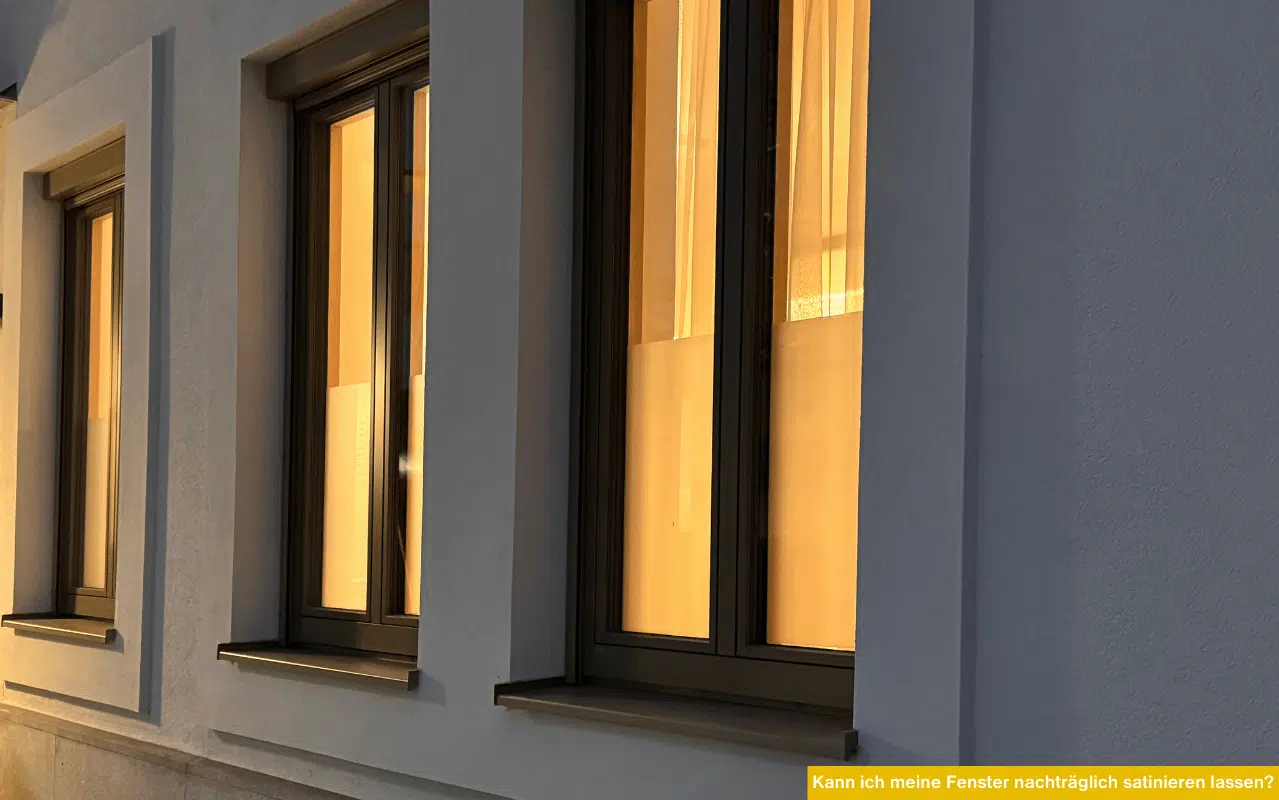 Kann ich meine Fenster nachträglich satinieren lassen? Abendliche Hausfassade mit beleuchteten Fenstern und teilweiser Sichtschutzwirkung durch nachträglich angebrachter Folie.