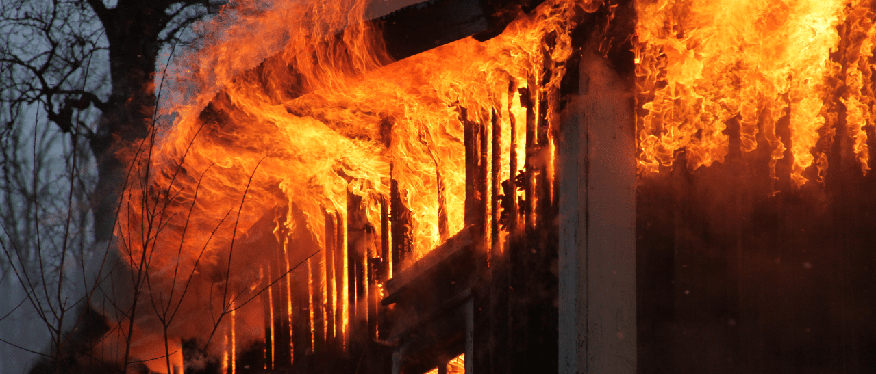 Das Foto zeigt ein brennendes Gebäude mit meterhohen Flammen. Es veranschaulicht eindrucksvoll, welche verheerenden Folgen fehlende Brandschutzfenster haben können, wenn sich Feuer unkontrolliert im Haus ausbreitet.