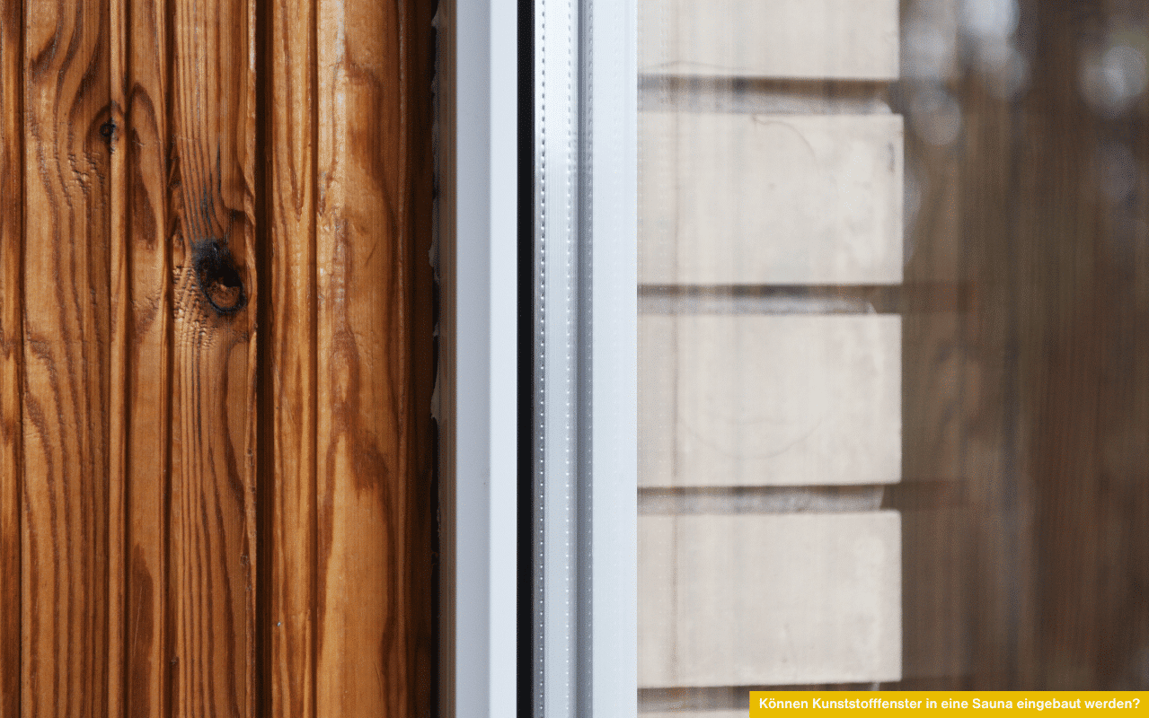 Können Kunststofffenster in eine Sauna eingebaut werden? Detailaufnahme eines weißen Kunststofffensters neben einer holzverkleideten Wand.
