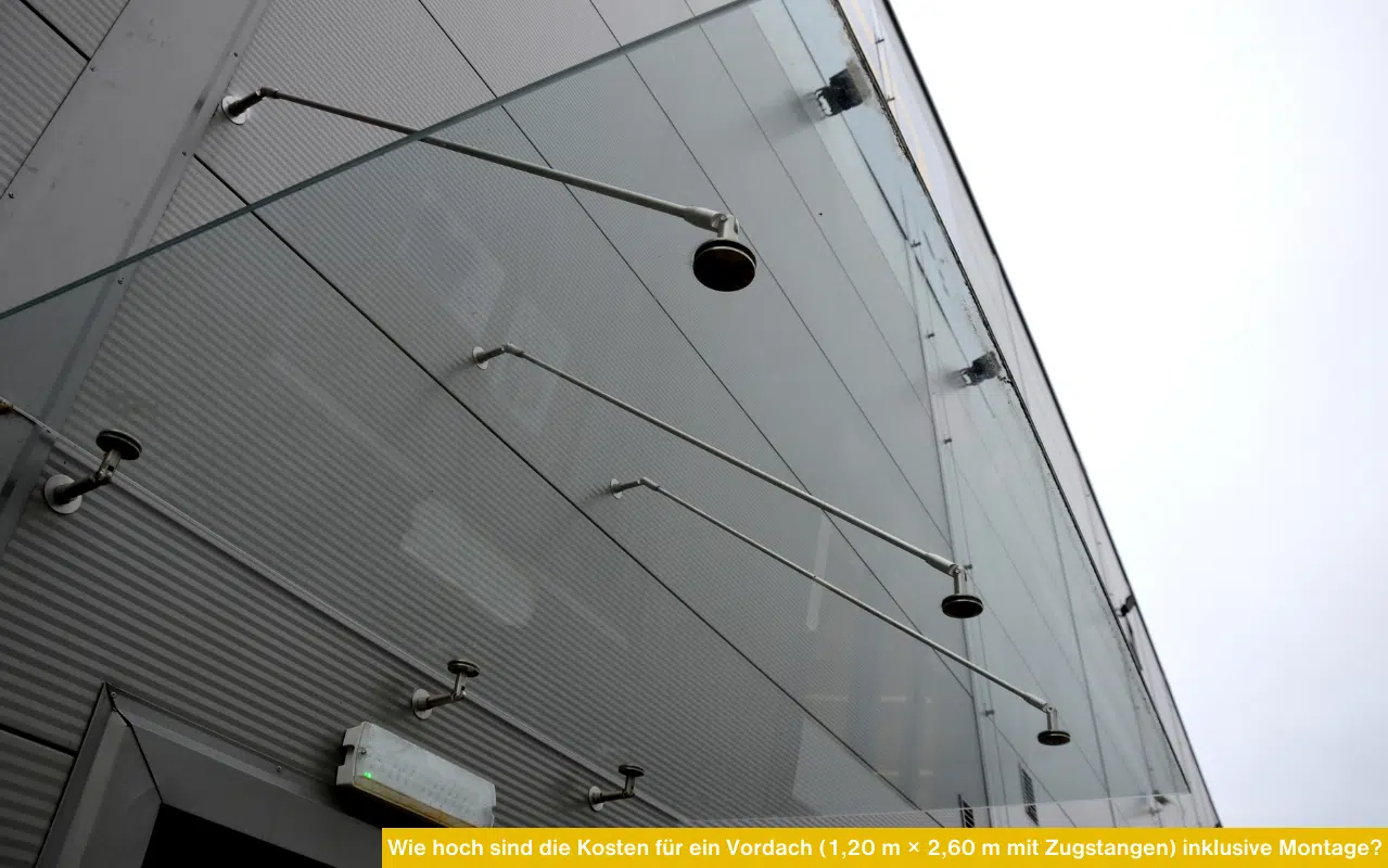Ein rahmenloses Glasvordach mit drei Edelstahl-Zugstangen und Wandhalterungen an einer modernen Wellblechfassade.