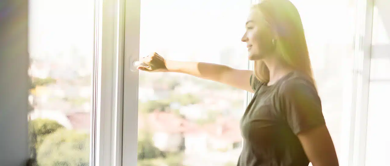 Frau öffnet Fenster, um durch Lüften Feuchtigkeit zu reduzieren, wenn die Scheiben schwitzen.