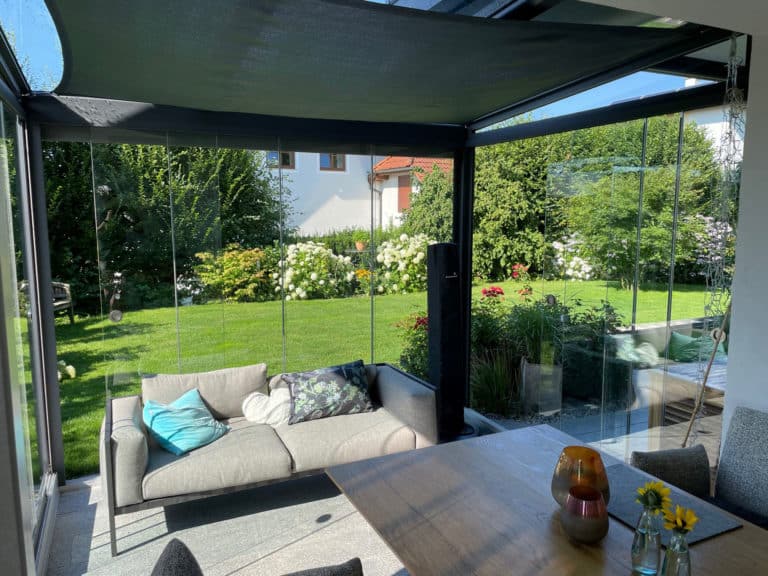 Blick aus dem Wintergarten durch die Glasschiebetüren auf Rasen und Blumenbeet