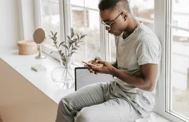 Materialien-ABC der Fensterbänke mit modernem Innenraum, großer Fensterbank und junger Person am Smartphone sitzend im Tageslicht