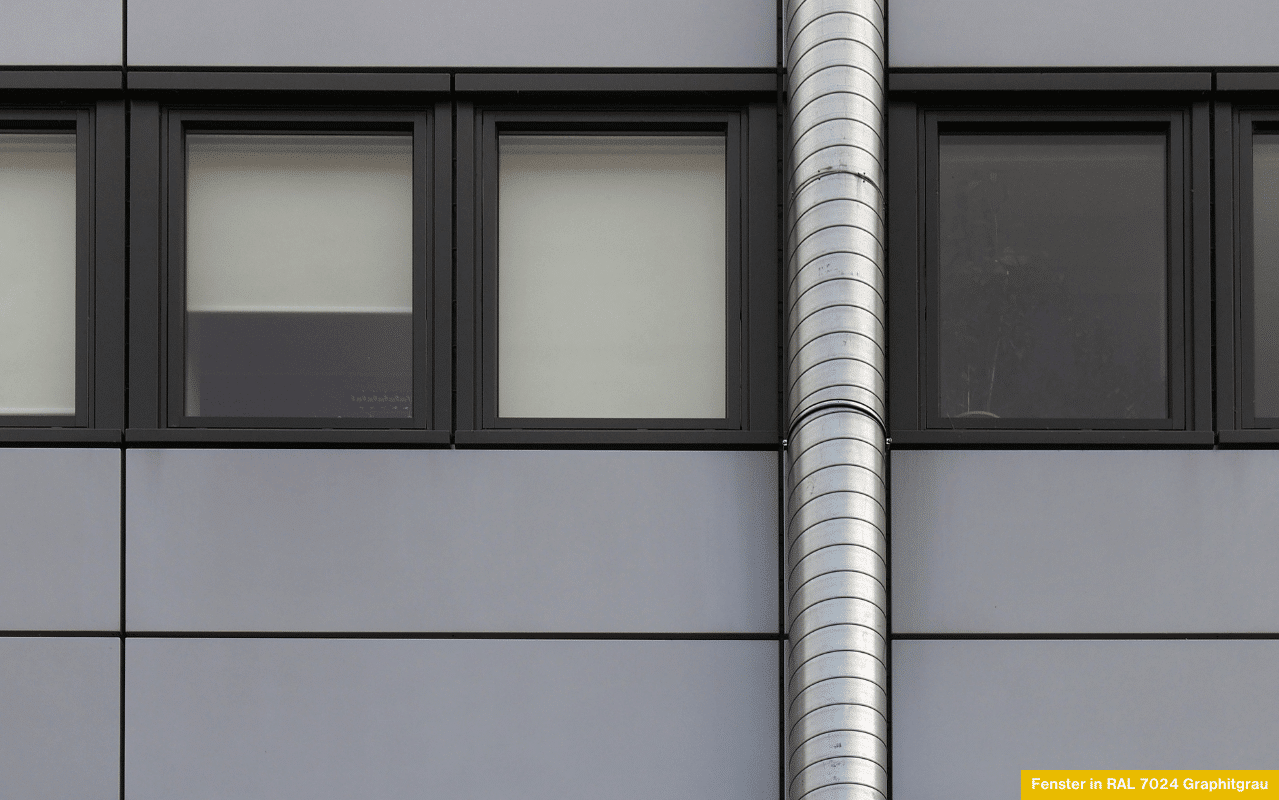 Das Bild zeigt eine moderne Gebäudeansicht mit rechteckigen Fenstern in RAL 7024 Graphitgrau. Der dunkle Grauton verleiht der klar strukturierten Fassade einen edlen, zeitlosen Charakter und harmoniert perfekt mit der Metalloptik.