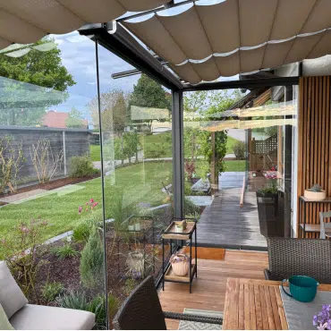 Moderne Pergola in Oberösterreich mit Glaswänden und Holzdetails – stilvolle Wohnraumerweiterung mit Blick in den Garten.