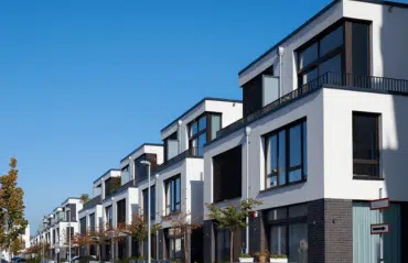 Das Bild zeigt eine moderne Häuserzeile mit klarer Architektur. Die großen Fensterrahmen in RAL 8016 Mahagonibraun setzen warme, elegante Akzente zur hellen, weißen Fassade und betonen den hochwertigen Stil der Gebäude.