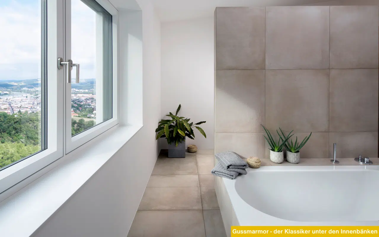Modernes Badezimmer mit Badewanne und Fenster. Weiße Innenfensterbank aus Gussmarmor. Blick auf Stadtlandschaft.