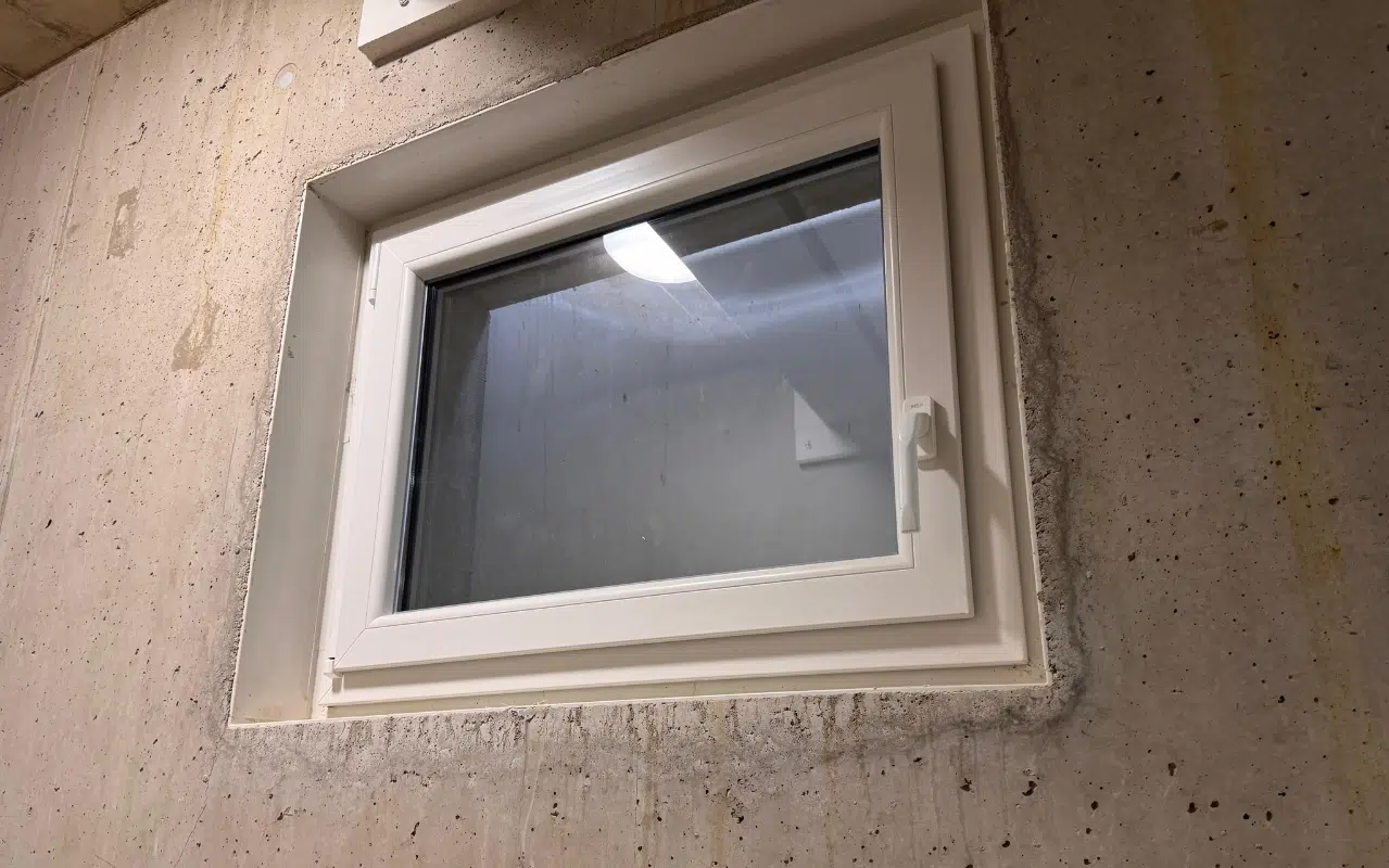 Modernes weißes Kunststoff-Kellerfenster in einer Betonwand für optimale Dämmung und Sicherheit im Haus