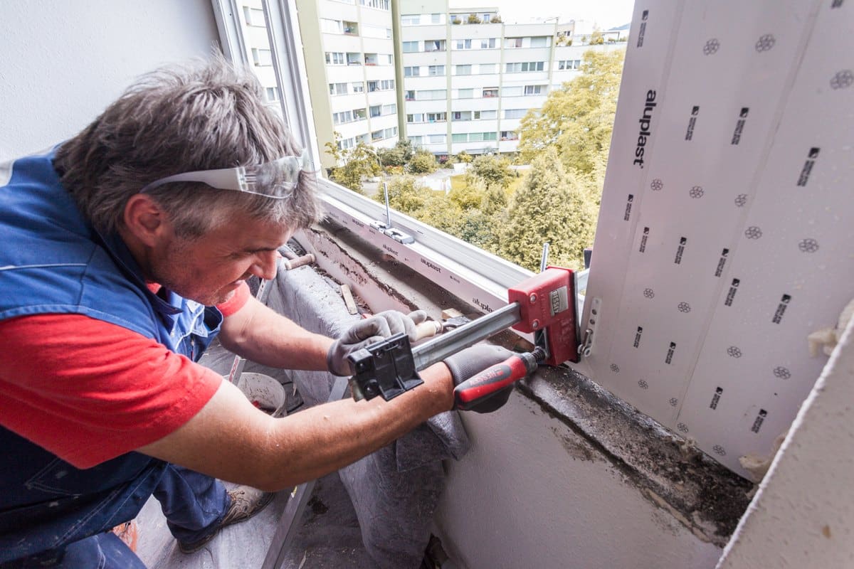 Monteur richtet den neuen Fensterrahmen mit Zwinge und Klotz aus, bevor er verschraubt wird
