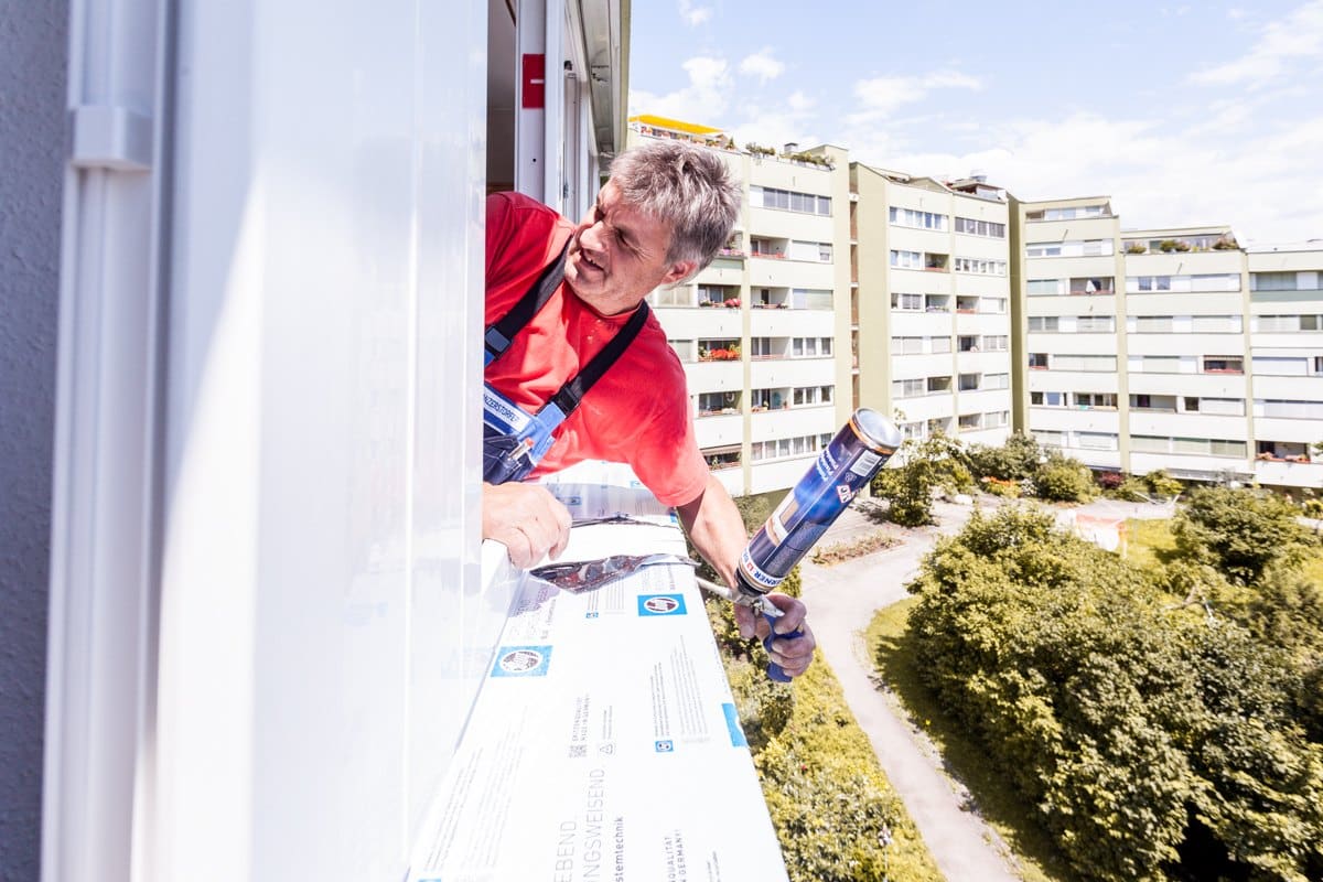 Monteur dämmt die Anschlussfuge zwischen Fensterrahmen und Mauerwerk von außen