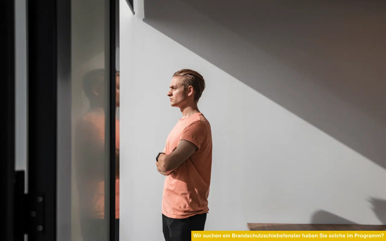 Person blickt aus einem modernen Fenster und steht stellvertretend für die Frage: Wir suchen ein Brandschutzschiebefenster, haben Sie solche im Programm?