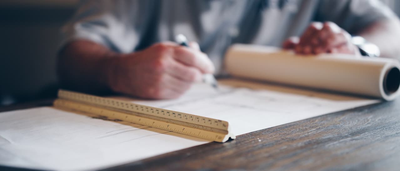 Das Bild zeigt einen Planer, der mit Lineal und Stift präzise Baupläne anfertigt. Es symbolisiert die sorgfältige Planung und Genehmigung von Poolhäusern, bei der technische Genauigkeit und Ästhetik Hand in Hand gehen.