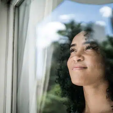 Frau schaut aus dem Fenster und fragt sich: Wie entwickeln sich die Fenster Preise 2023? Mehr dazu im Beitrag.