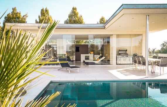 Rahmenlose Glas-Schiebetüren von Sunflex SF 20 an einem Poolhaus im Garten – luftige Atmosphäre durch großflächige Glasflächen ohne sichtbare Rahmenkonstruktion.