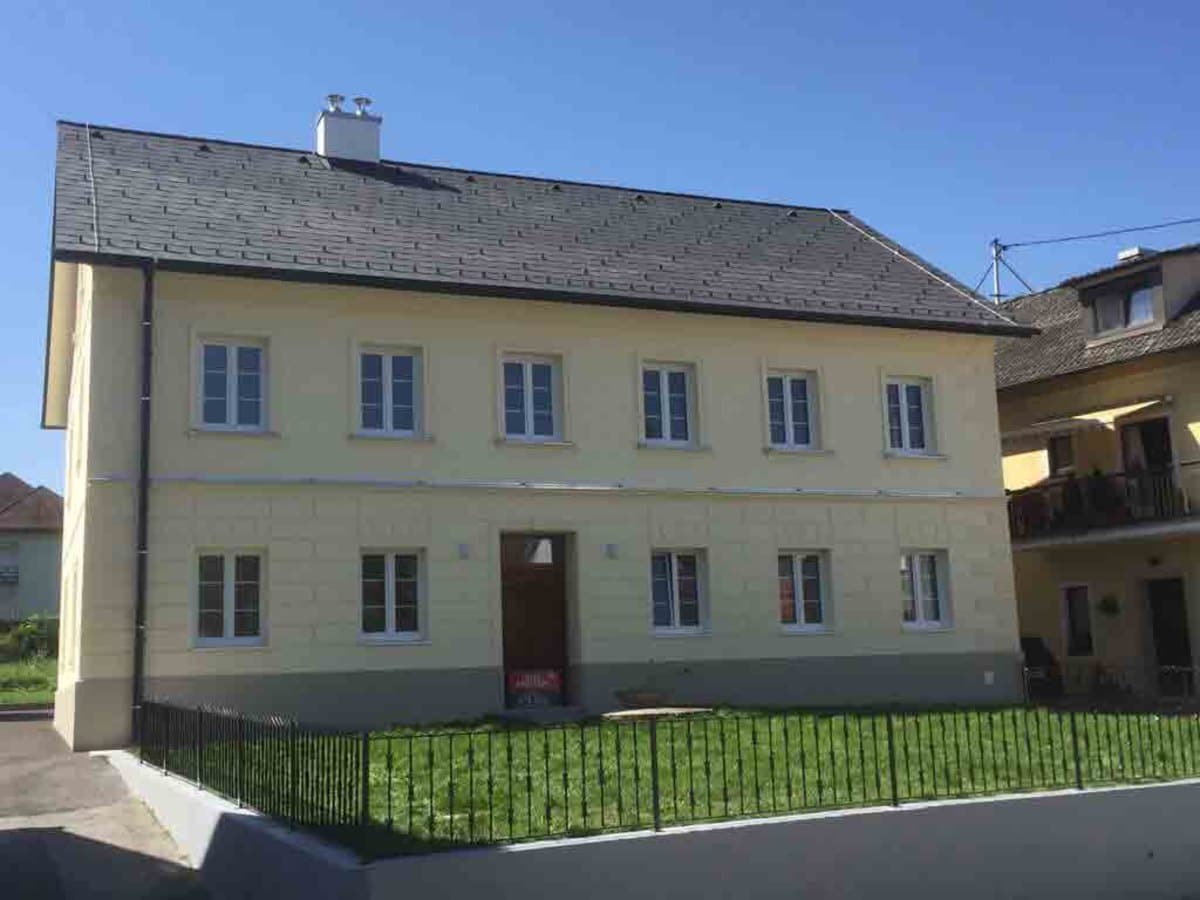 Renoviertes zweigeschoßiges Haus mit gelber Fassade und neuen weißen Sprossenfenstern