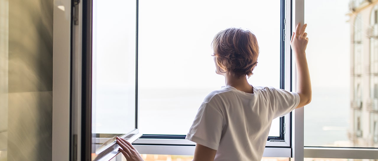 Das Bild zeigt eine Frau, die ein Fenster öffnet, um richtig zu lüften. Es verdeutlicht den positiven Effekt von Frischluft auf das Raumklima und die Wohnqualität.