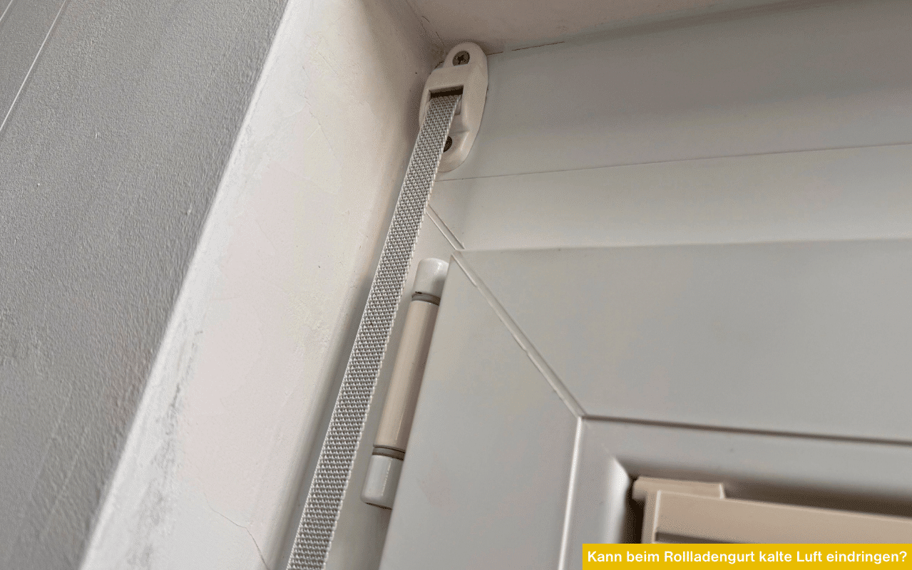 Detailaufnahme einer Gurtführung für Rollläden an einem weißen Kunststofffenster; Fokus auf die mechanischen Durchlässe.