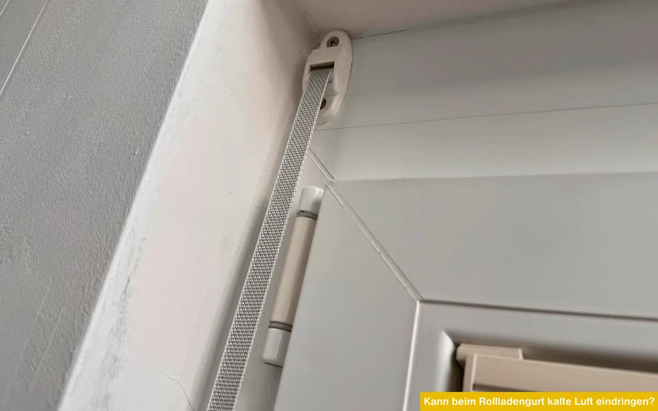 Detailaufnahme einer Gurtführung für Rollläden an einem weißen Kunststofffenster; Fokus auf die mechanischen Durchlässe.