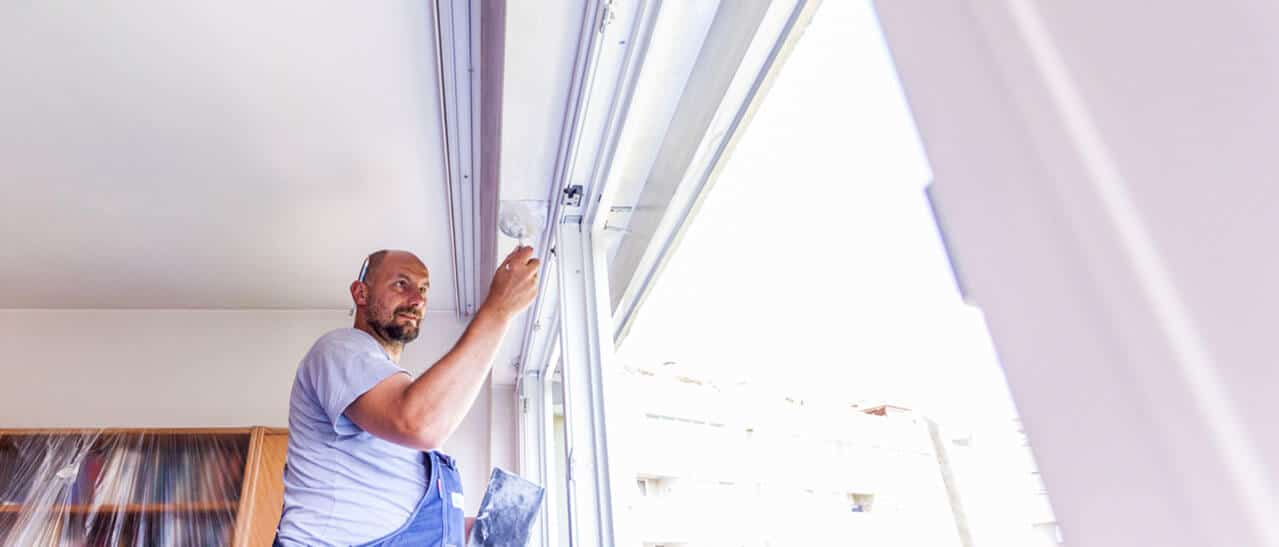 Sanierungsscheckt 2017 - Das Bild zeigt einen Handwerker von Fenster-Schmidinger in einer blauen Latzhose und einem grauen T-Shirt bei der Montage eines großflächigen Fensters oder einer Balkontür.
