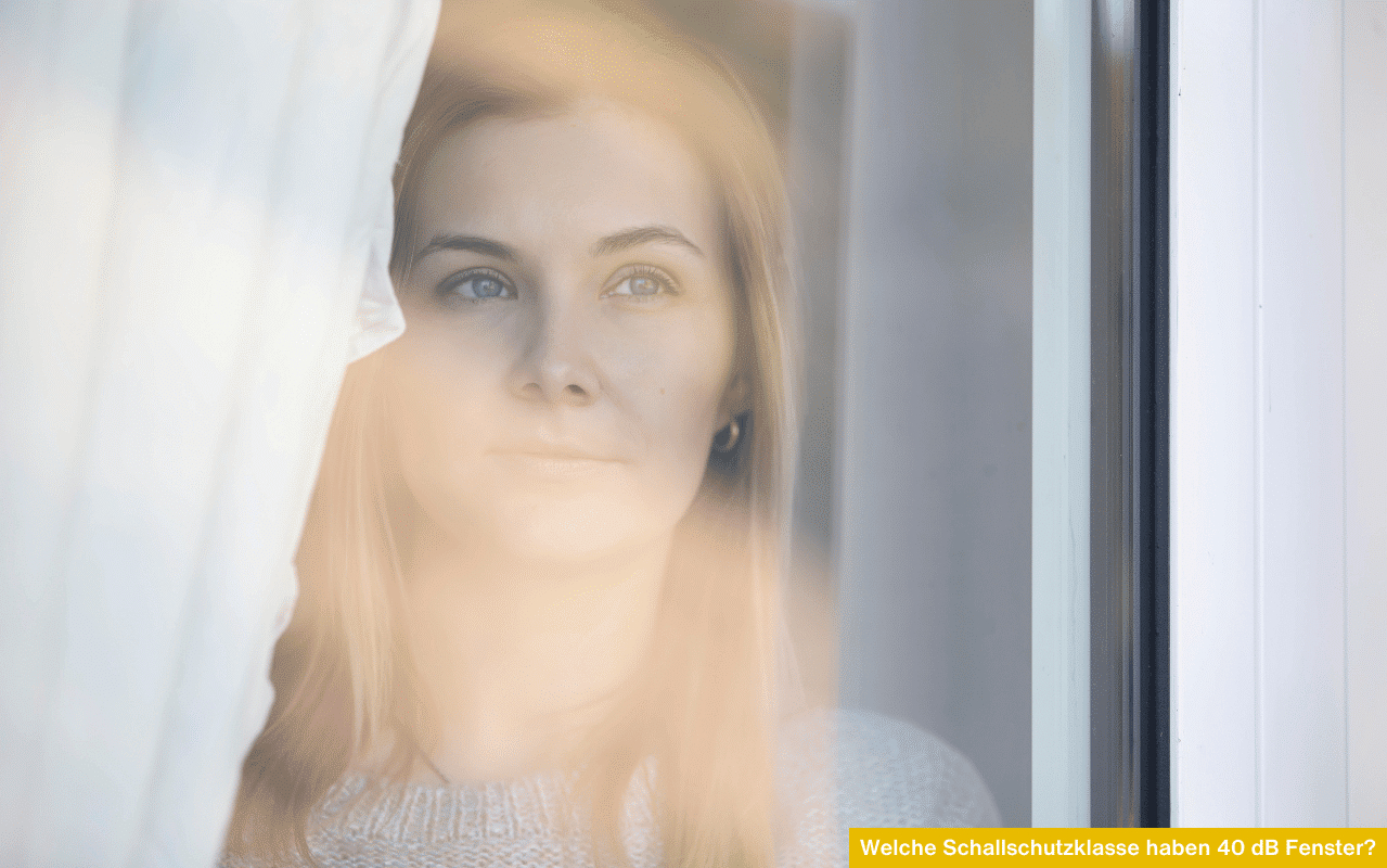 Porträt einer jungen Frau, die ruhig hinter einer Fensterscheibe ins Freie blickt - Thema Schallschutzklasse 4.