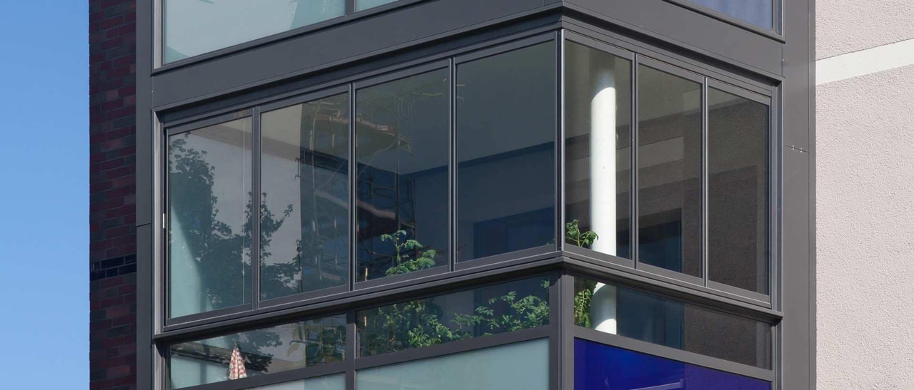 Schiebe-Dreh Schallschutzverglasung Balkon mit Aluminiumrahmen und teiltransparenter Verglasung für Lärmschutz und Wetterschutz.